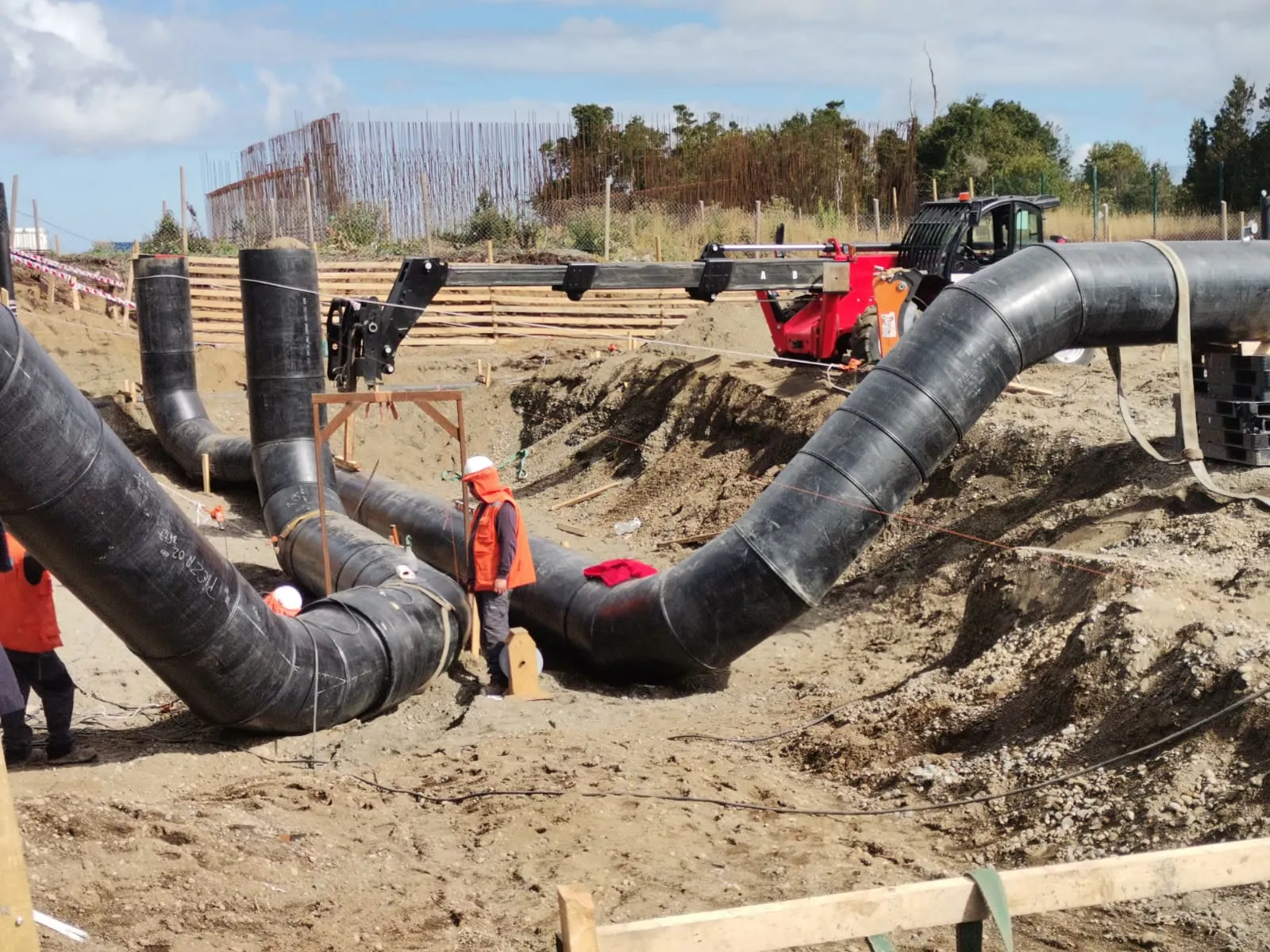 Codos de tubería HDPE de gran diámetro montados en una zanja, con un operario con casco y chaleco reflectante trabajando al lado.